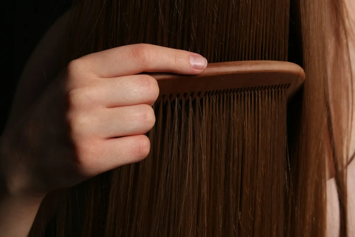 A hand runs a wooden comb through long brown hair.